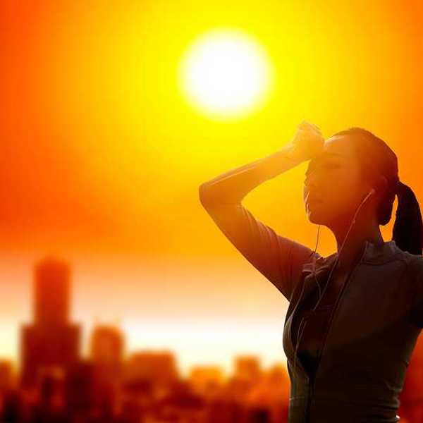 Woman shielding her eyes from sun with summer heat wave in the city background.