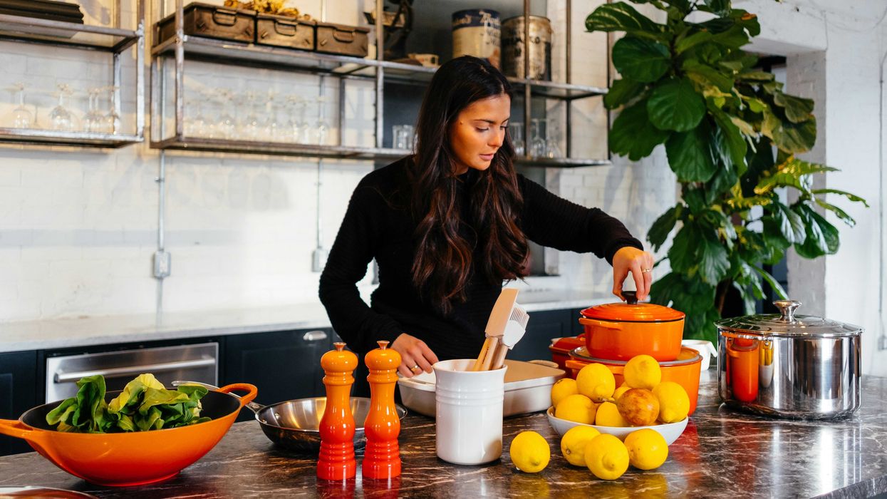 woman standing in front of fruits holding pot's lid.