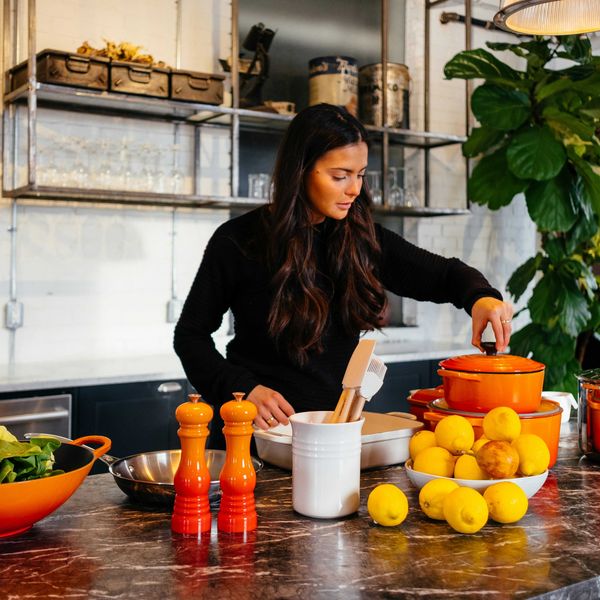 woman standing in front of fruits holding pot's lid.