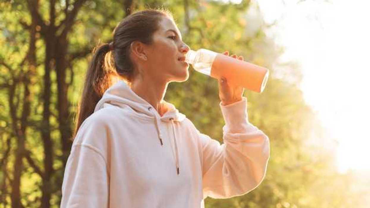 Woman wearing a pink sweatshirt drinking water out of a reusable bottle