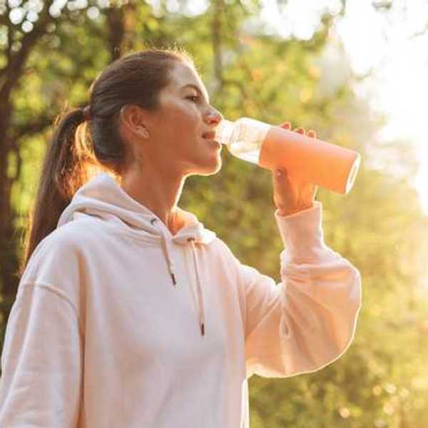 Woman wearing a pink sweatshirt drinking water out of a reusable bottle