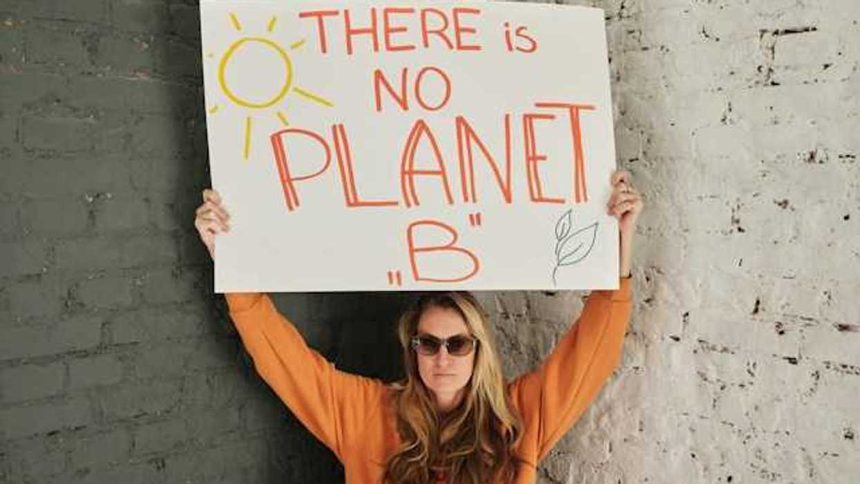 Woman wearing an orange sweatshirt holding a sign saying There is no planet B