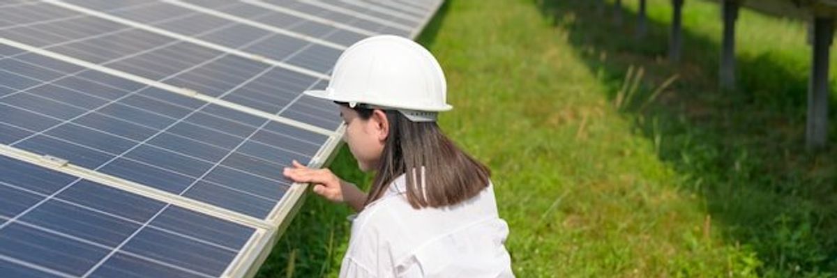 Woman wearing hard hat inspecting solar panels in a field.