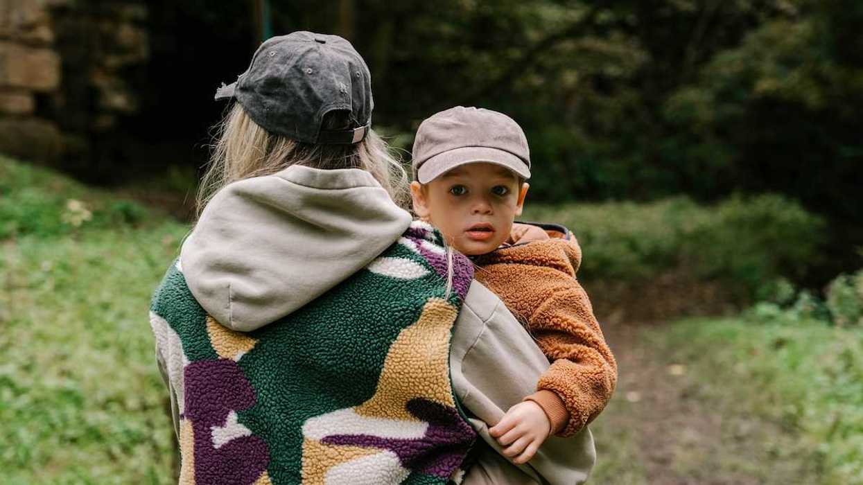 Woman wearing patterned fleece vest holding child wearing orange-brown fleece pullover