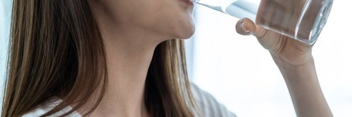 Woman with long brown hair drinking a glass of water.