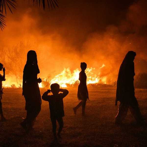 Women and children silhouetted against fire