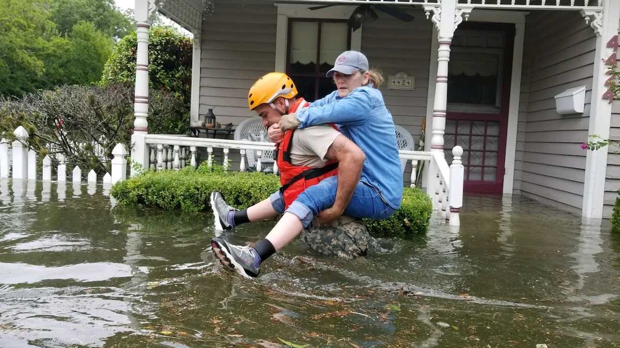 Women riding on back of rescue worker in flooded street outside home