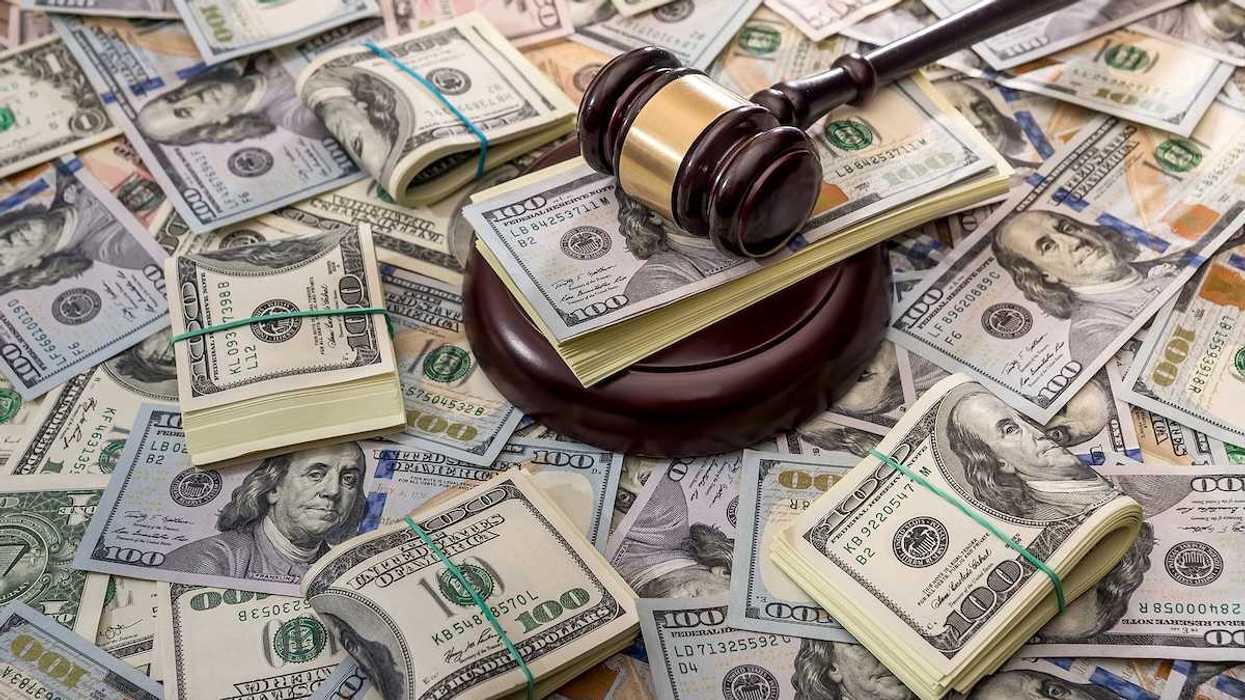 Wooden court gavel overlaying and surrounded by hundred-dollar bills