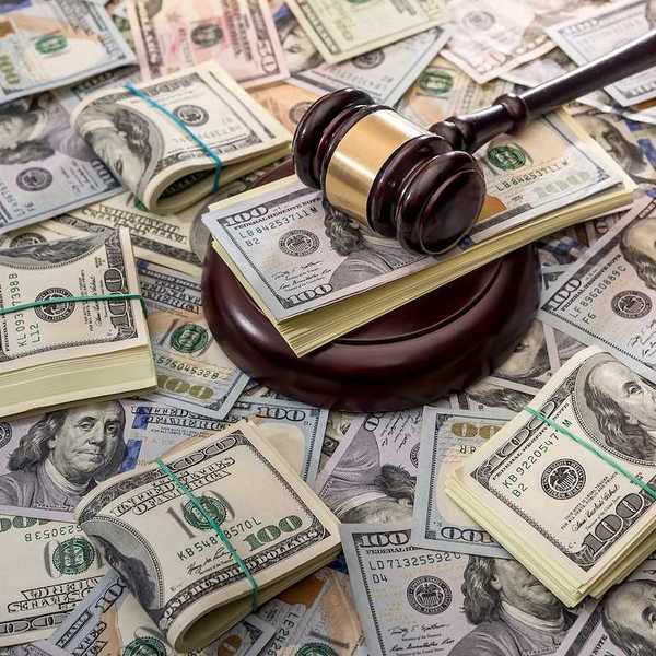 Wooden court gavel overlaying and surrounded by hundred-dollar bills