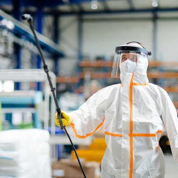 Worker in hazmat suit spraying a room
