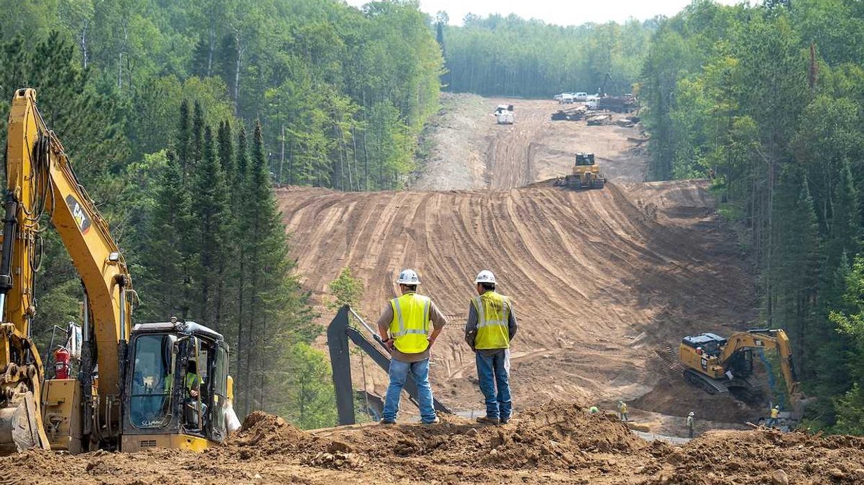 Workers overlook the Enbridge Line 3 Oil Pipeline Construction Site in Minnesota forest with excavators and bulldozer.