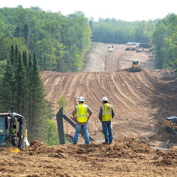 Workers overlook the Enbridge Line 3 Oil Pipeline Construction Site in Minnesota forest with excavators and bulldozer.