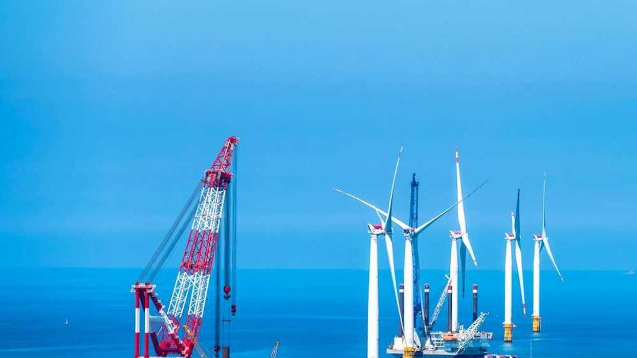 Yellow and white offshore wind turbines being installed using a floating red & white crane