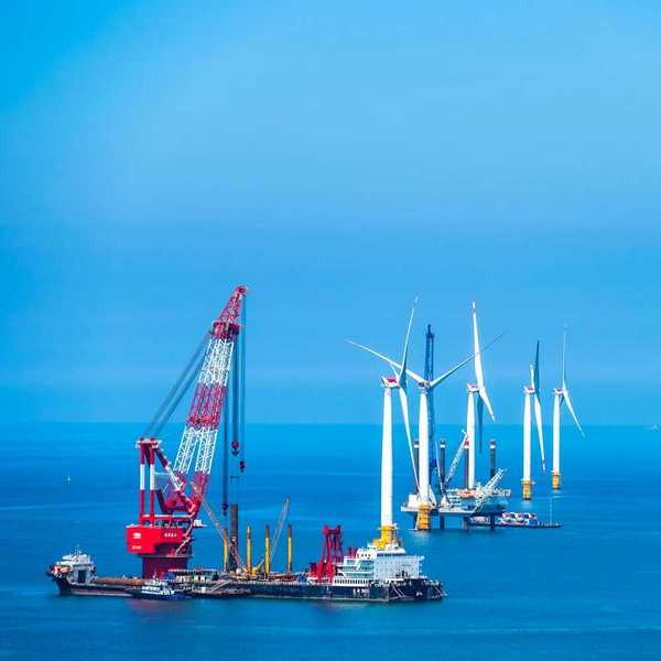 Yellow and white offshore wind turbines being installed using a floating red & white crane
