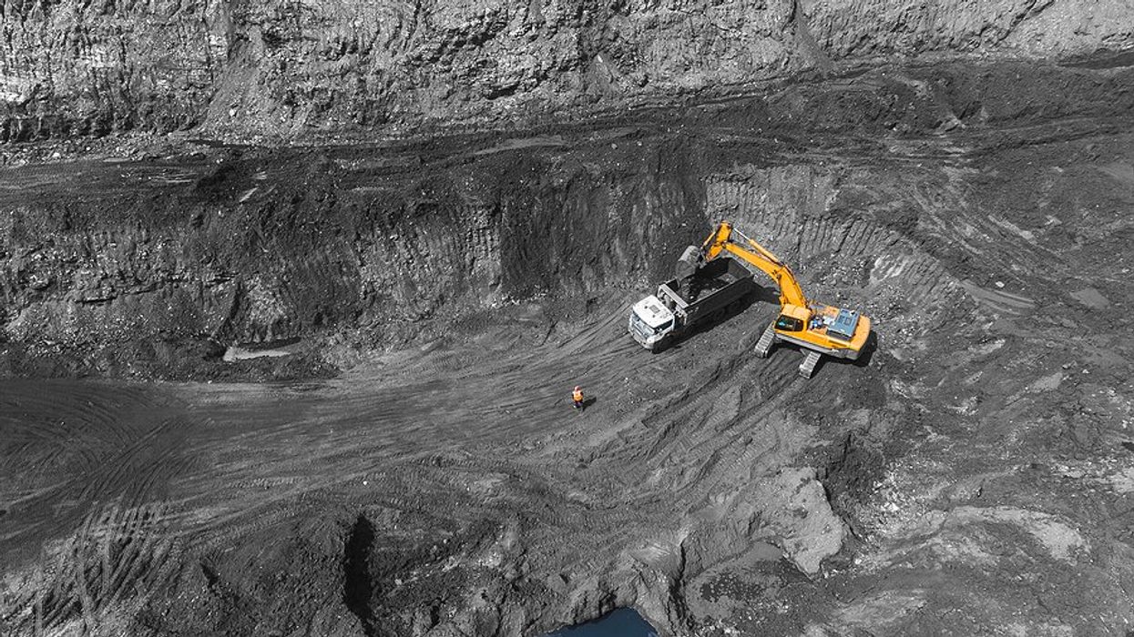 Yellow excavator loading rock truck in open pit coal mine