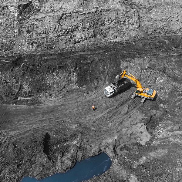 Yellow excavator loading rock truck in open pit coal mine