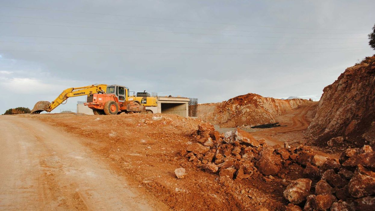 yellow excavator near brown rock formation during daytime