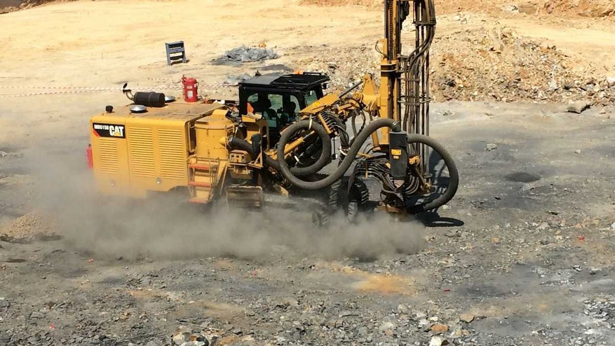 Yellow mining equipment drilling into rock and raising dust