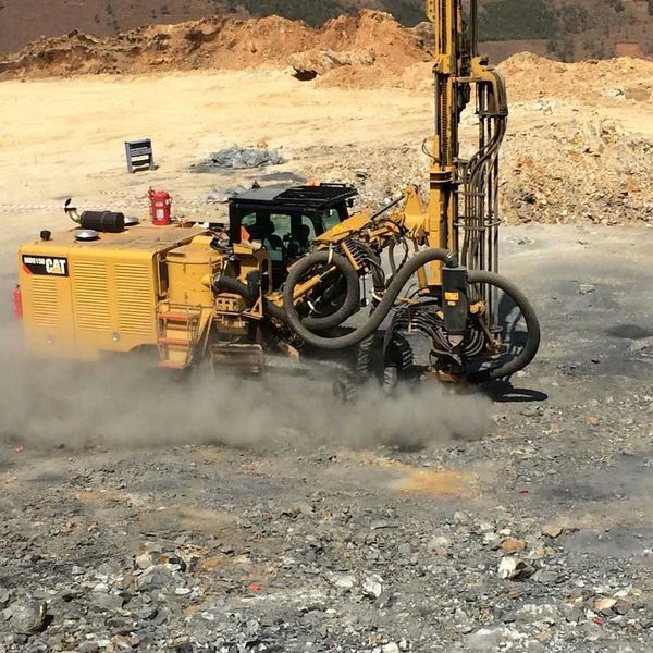Yellow mining equipment drilling into rock and raising dust