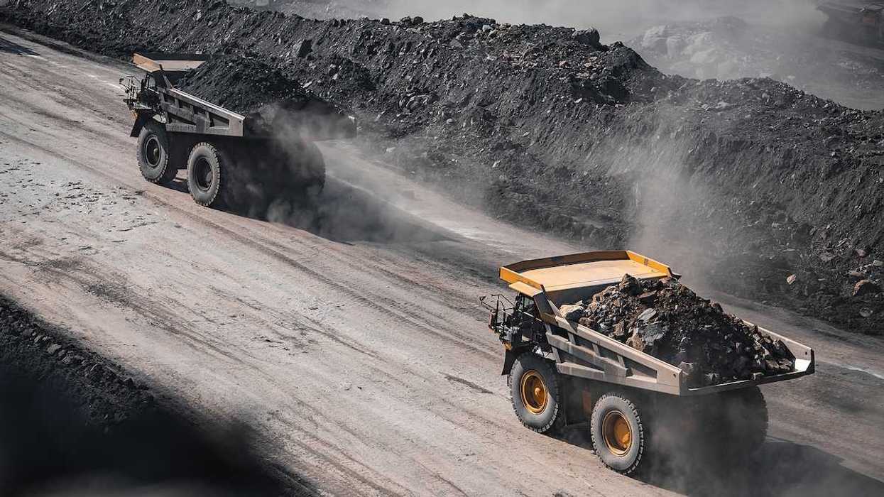 Yellow mining trucks moving along a dusty quarry road while working an open pit coal mine.
