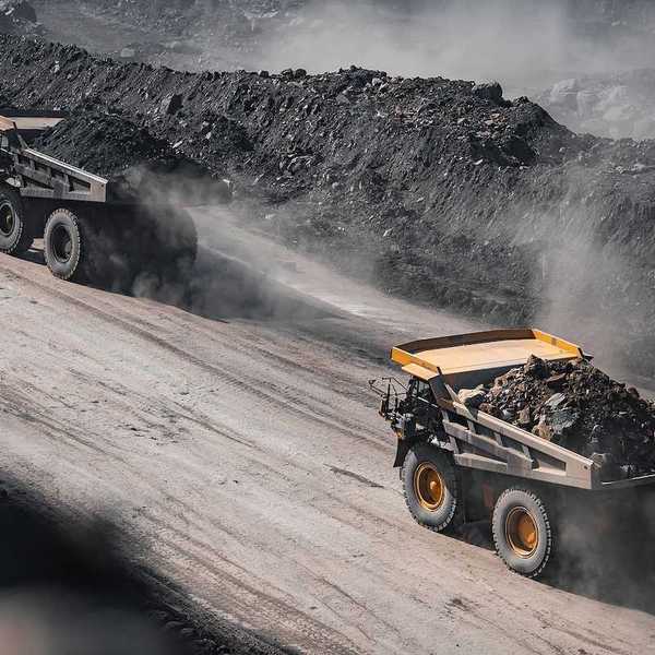 Yellow mining trucks moving along a dusty quarry road while working an open pit coal mine.