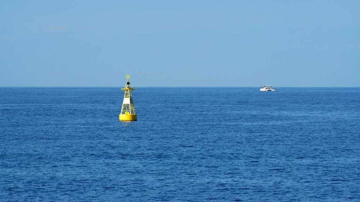 Yellow ocean monitoring buoy with an unidentified white boat nearby