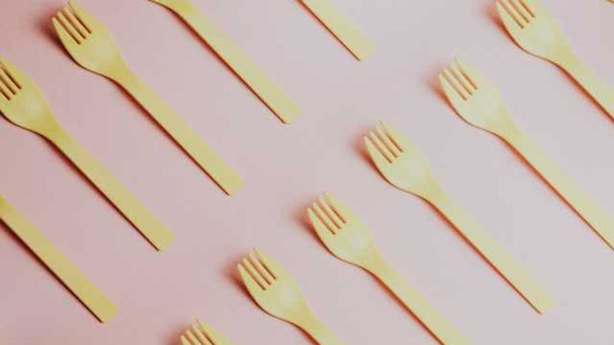 Yellow plastic forks lined up diagonally against a pink background