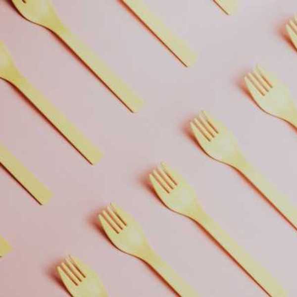 Yellow plastic forks lined up diagonally against a pink background