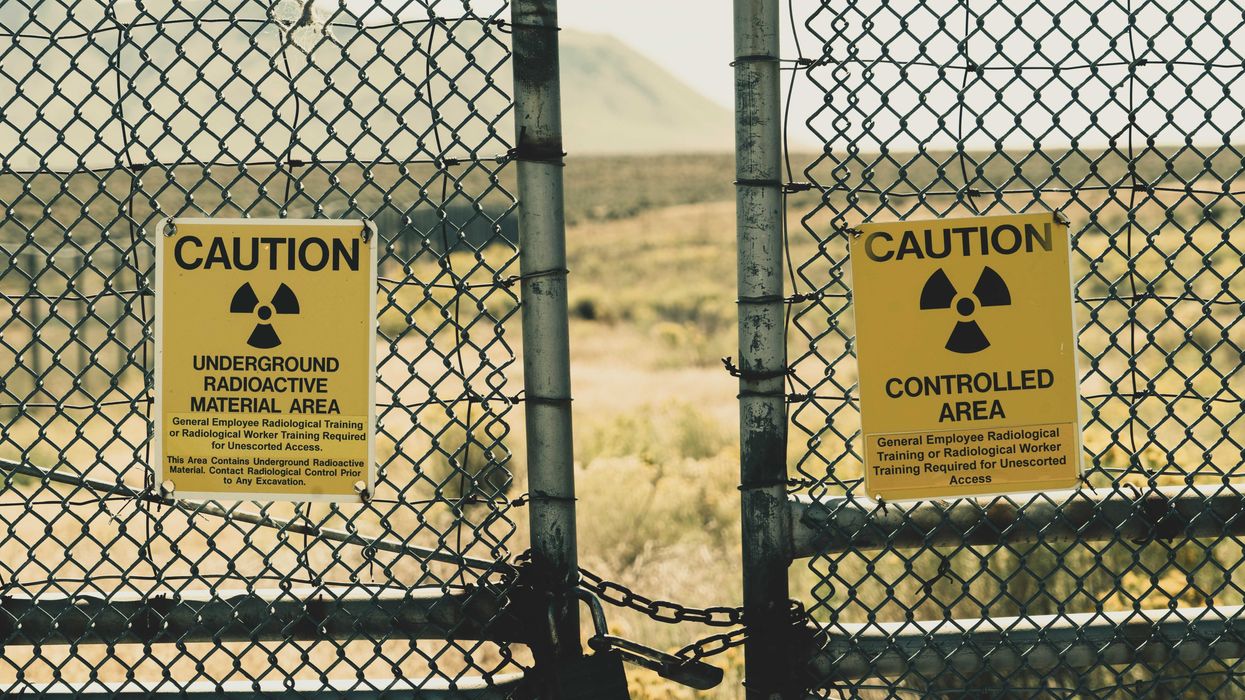 yellow radioactive material warning sign posted on a fence with mountains in background.