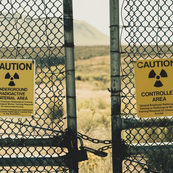 yellow radioactive material warning sign posted on a fence with mountains in background.