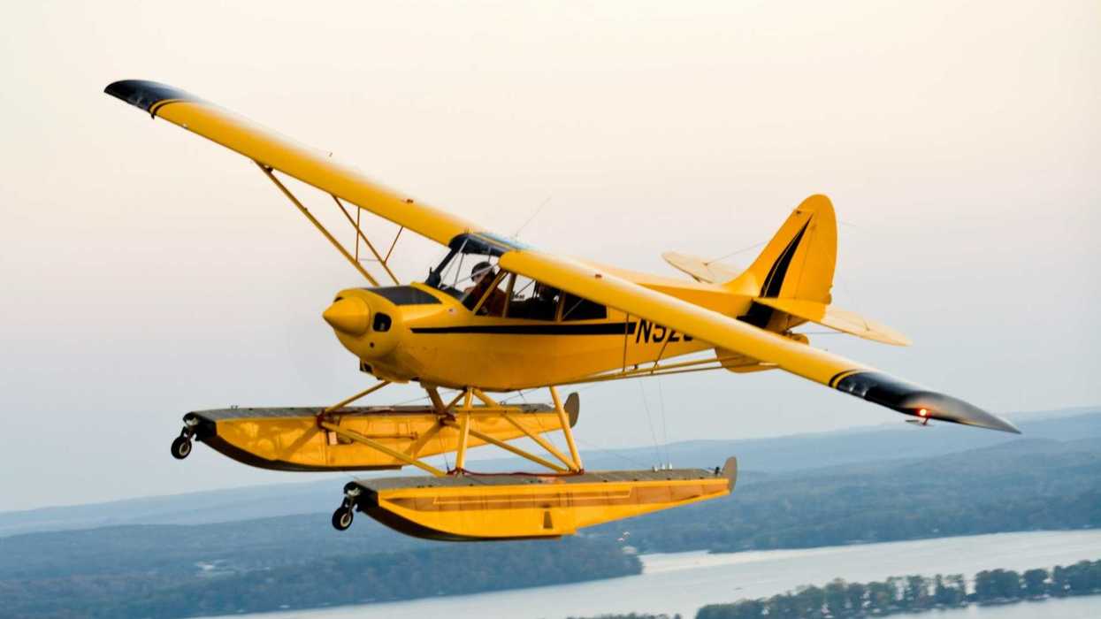 Yellow sea plane flying over a waterbody in a forested country