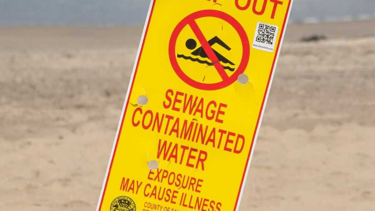 Yellow sign with red lettering reads "KEEP OUT, SEWAGE CONTAMINATED WATER. EXPOSURE MAY CAUSE ILLNESS"