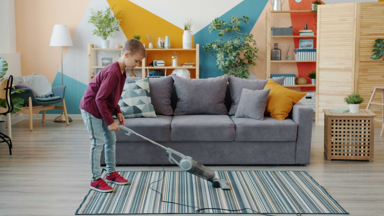 Young boy vacuuming a striped rug in a colorful living room.
