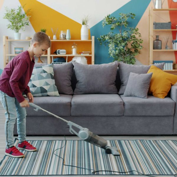 Young boy vacuuming a striped rug in a colorful living room.