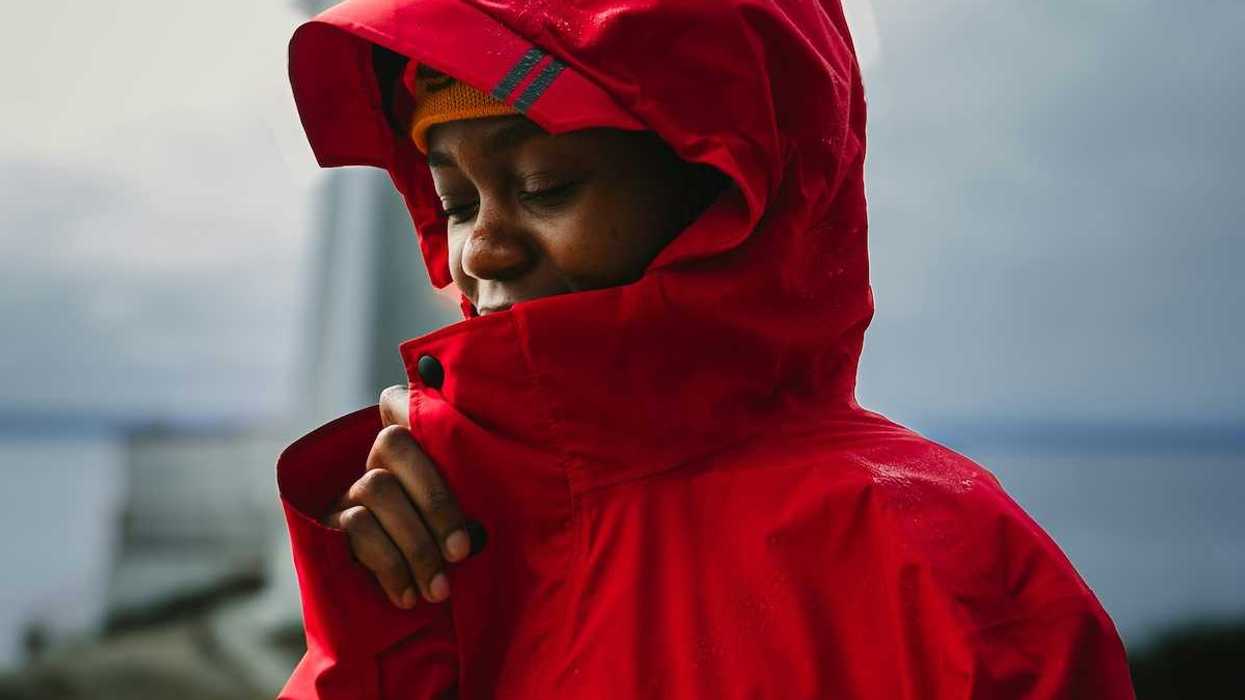 Young brown-skinned boy snuggled into red rain jacket with hood