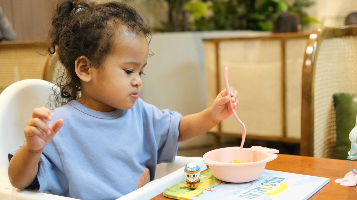 Young child eating with a pink spoon and bowl.