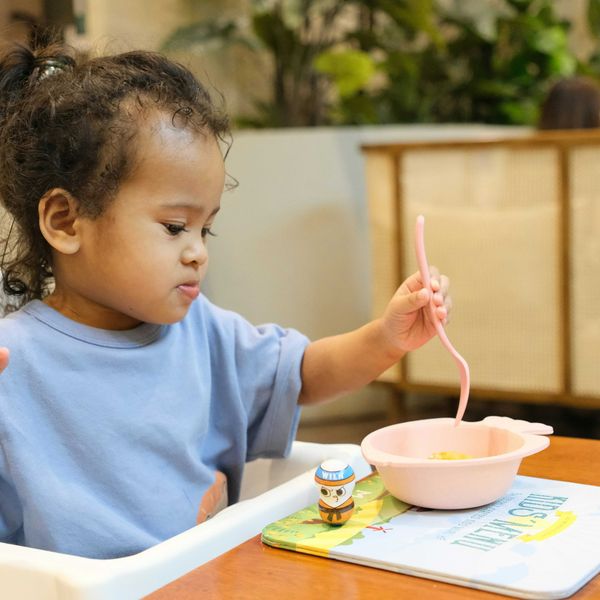 Young child eating with a pink spoon and bowl.
