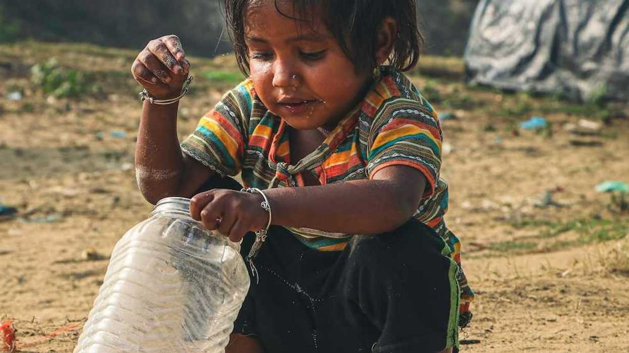 Young child squatting in the dirt, adding coins to a plastic jar