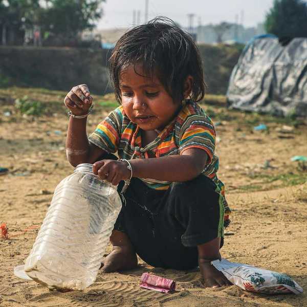 Young child squatting in the dirt, adding coins to a plastic jar