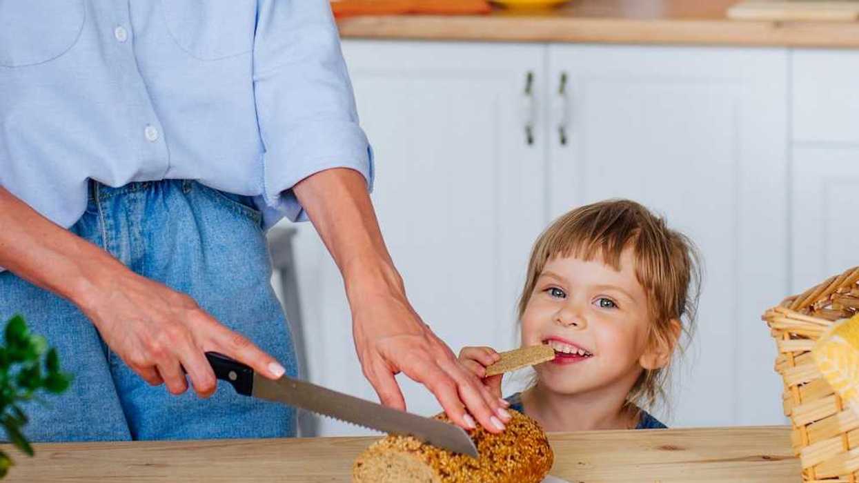 Young girl eating a cracker while woman slices bread