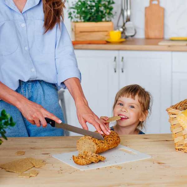 Young girl eating a cracker while woman slices bread