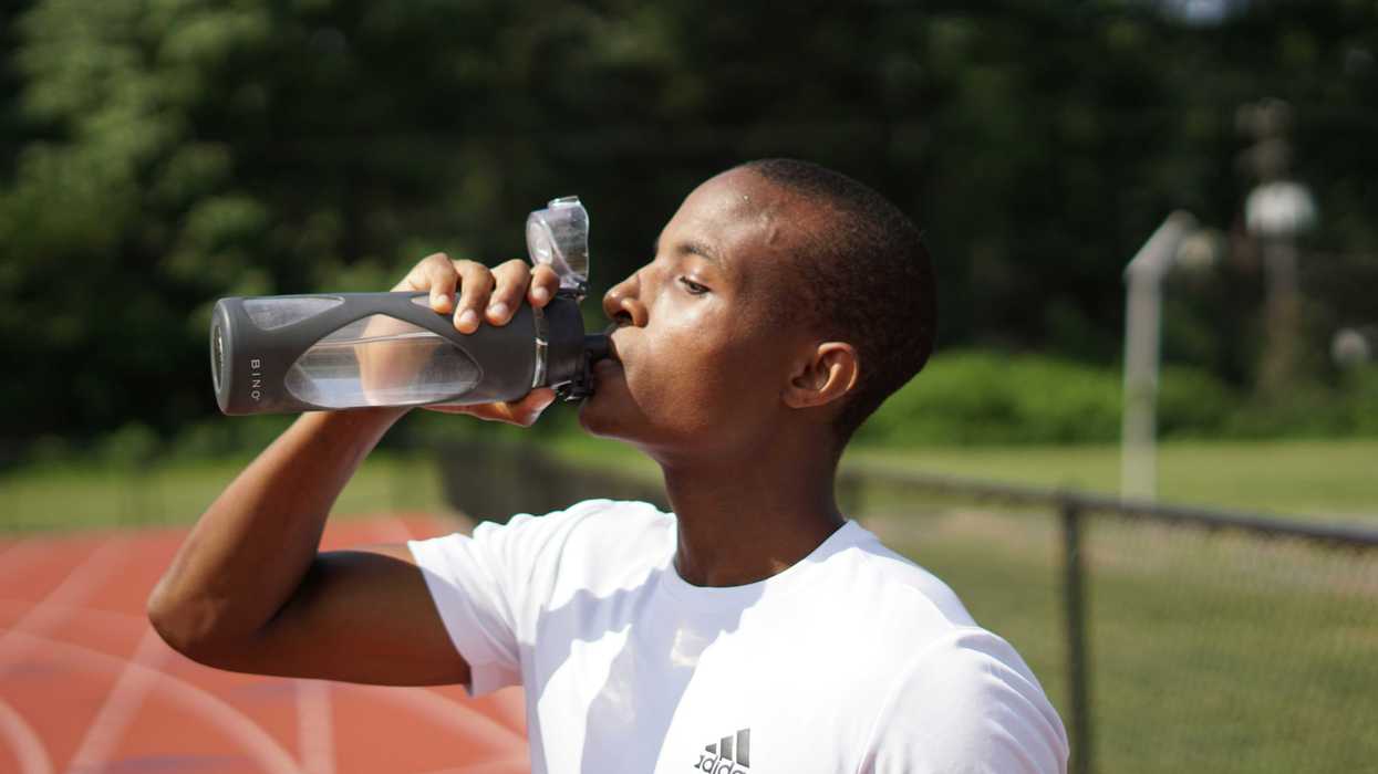 Young man in white crew neck t-shirt drinking from plastic sports bottle.