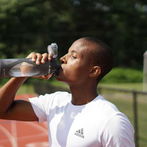 Young man in white crew neck t-shirt drinking from plastic sports bottle.