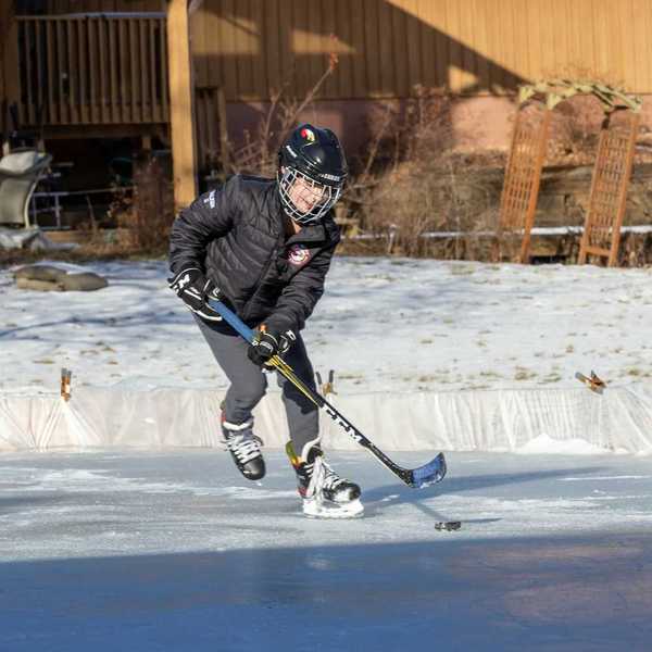Young person winter-skating on backyard rink with hockey stick and puck