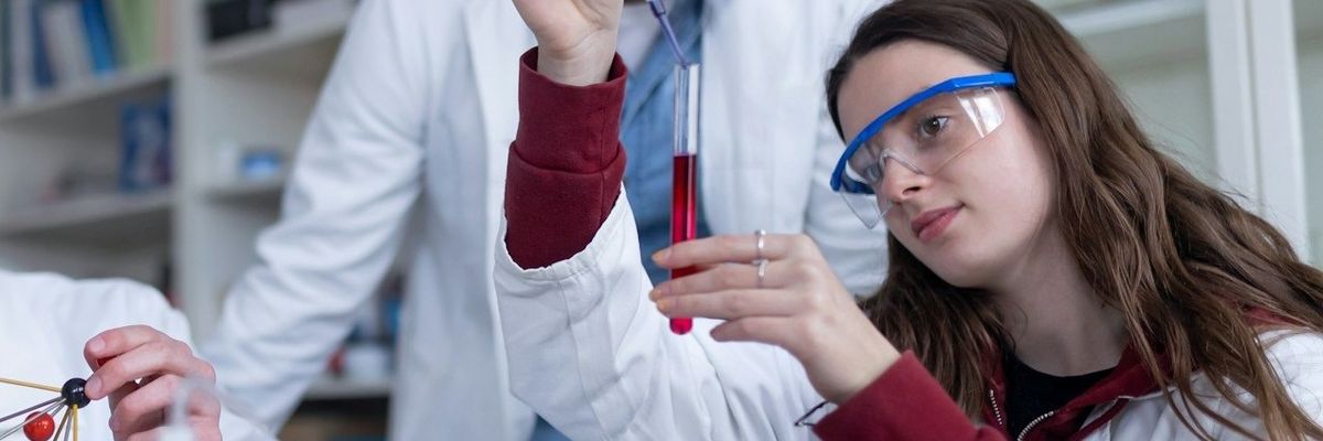 Young scientists and instructor filling test tubes with a red liquid at a lab table.