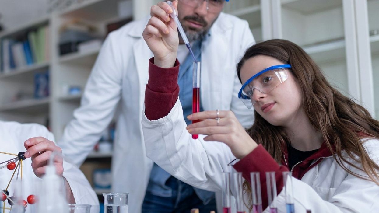 Young scientists and instructor filling test tubes with a red liquid at a lab table.