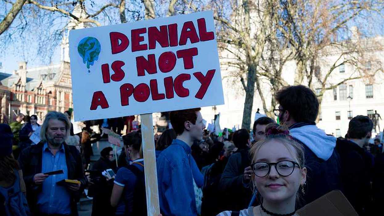 Young woman holding sign of protest reading "DENIAL IS NOT A POLICY."