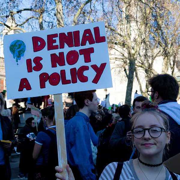 Young woman holding sign of protest reading "DENIAL IS NOT A POLICY."