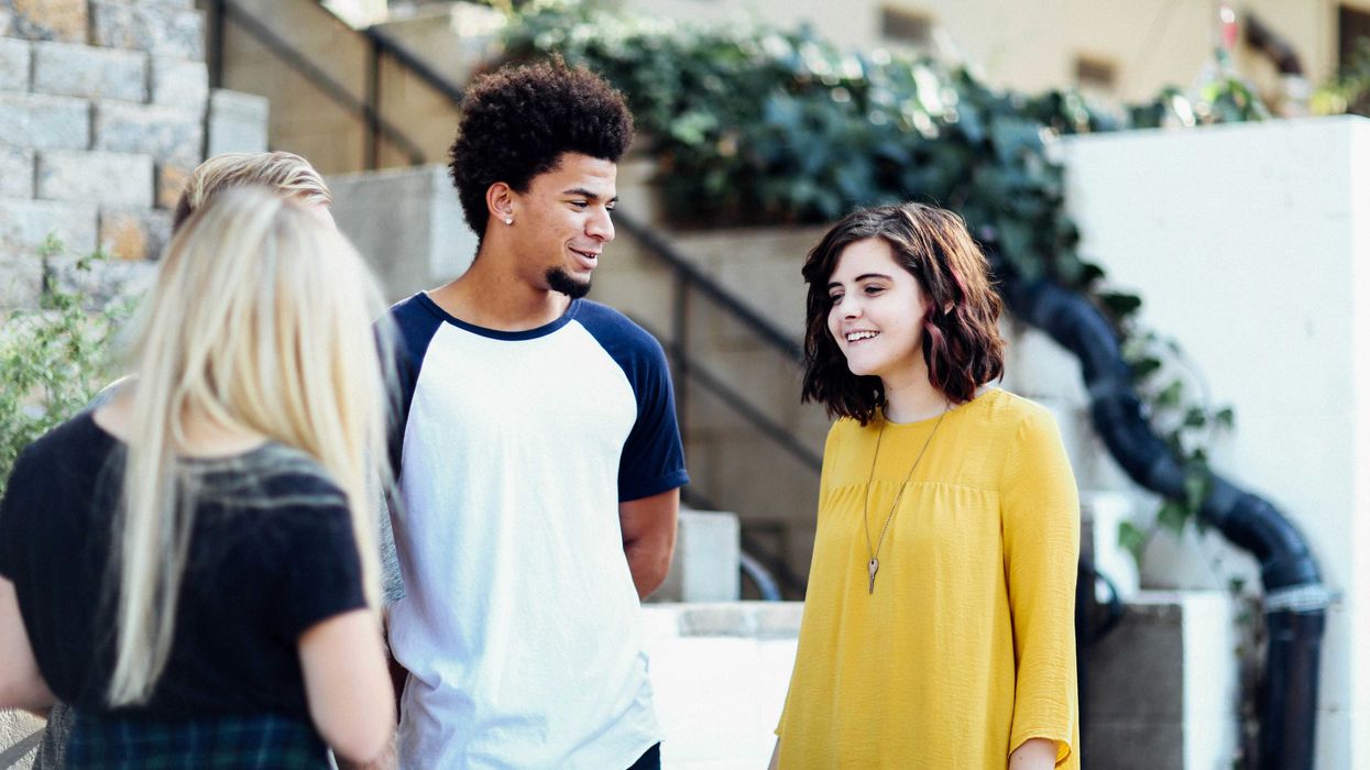 Young women and man talking and smiling outside a building.